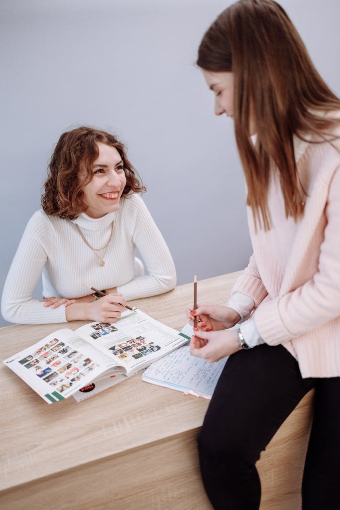 Two women engaging in a vibrant study session with books in a classroom setting.